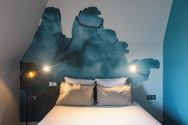 A bedroom with a bed, two bedside lamps, and a wall mural.