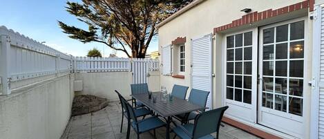 A patio with a table and chairs, a white fence, and a tree.