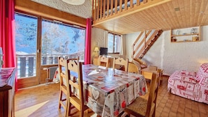 A cozy room with a wooden dining table, chairs, a sofa, and a staircase leading to an upper level. - Cozy Duplex in La Clusaz - 5 pers, pets allowed (La Clusaz)