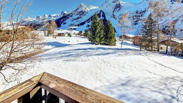 A snowy mountain landscape with a clear sky, a wooden deck, and a few buildings in the background. - Cozy Duplex in La Clusaz - 5 pers, pets allowed (La Clusaz)