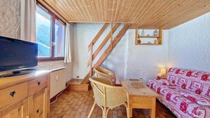 A cozy room with a wooden ceiling, a TV on a cabinet, a wicker chair, a wooden table, and a patterned sofa. - Cozy Duplex in La Clusaz - 5 pers, pets allowed (La Clusaz)