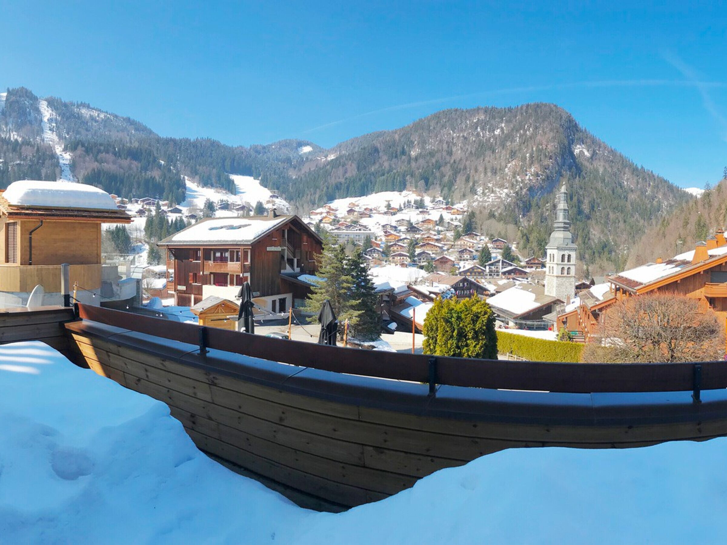 Un bote de madera sobre nieve, con vista a un pueblo montañoso con edificios y una iglesia.