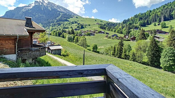 A mountain village with traditional wooden houses, a wooden fence, and a clear view of a mountain in the background.