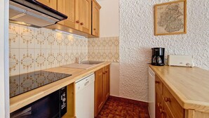 A compact kitchen with wooden cabinets, a dishwasher, a coffee maker, and a map on the wall. - Cozy studio in La Clusaz, 4 pers, pets allowed (La Clusaz)