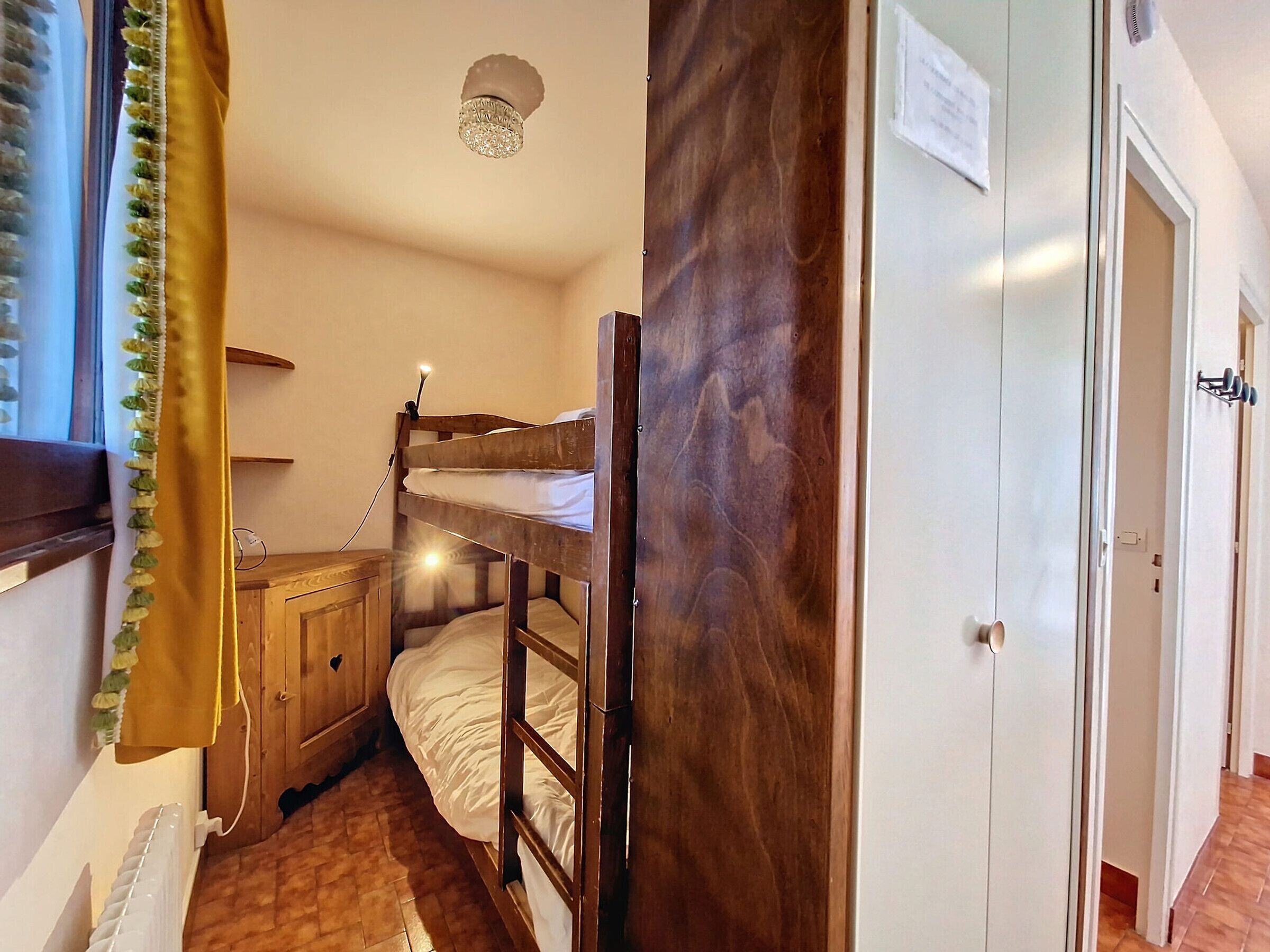 A small, cozy room with a bunk bed, wooden wardrobe, and a radiator.