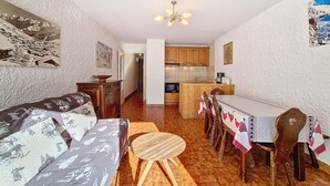 A cozy living room with a sofa and a dining table set for four, a kitchen in the background, and a hallway leading to another room. - Cozy studio in La Clusaz, 4 pers, pets allowed (La Clusaz)