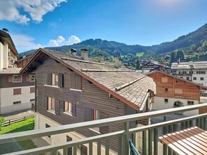 A traditional wooden building with a sloped roof, a balcony, and a view of a mountainous landscape.