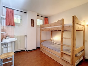 Habitación con literas de madera, un lavabo y una ventana con cortinas.