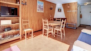 Ein Zimmer mit Holzwänden, einem Fernseher, einem Esstisch mit Stühlen, einer Couch und einem Kamin.
