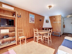 Una habitación con paneles de madera, un televisor, una mesa de comedor con sillas, un sofá y una chimenea.