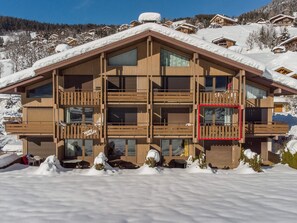 A wooden chalet with multiple balconies and large windows, surrounded by snow-covered mountains.