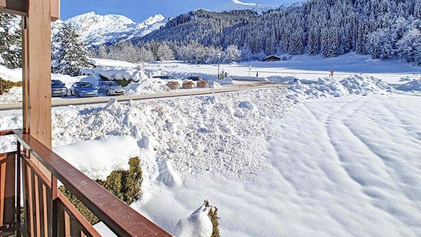 A snowy mountain landscape with a clear sky, a road with parked cars, and a building in the distance.