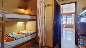 A bunk bed room with a wooden headboard, a small shelf, and a bedside table with a lamp.