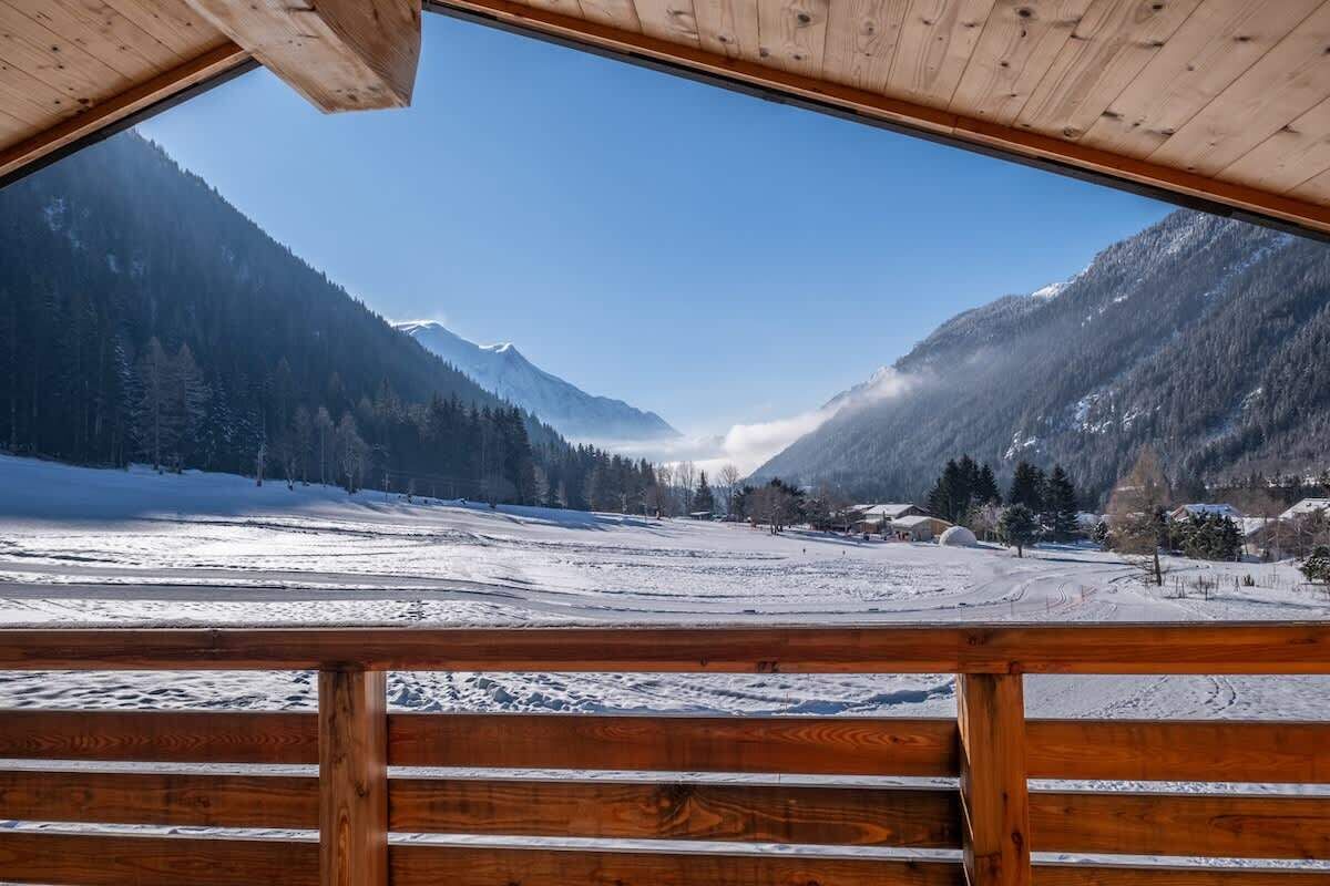 Uitzicht vanaf een houten balkon op een besneeuwde vallei met bergen.