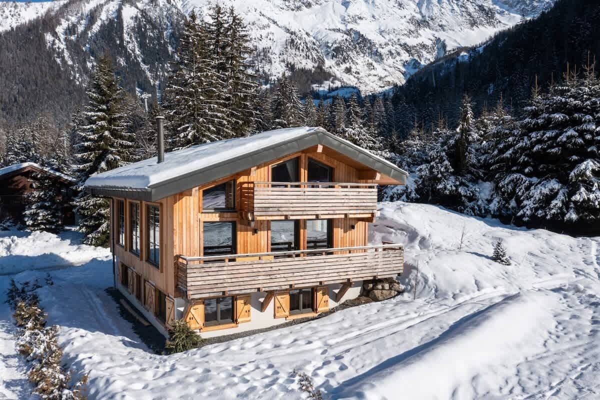 Une cabane en bois dotée d’un balcon, entourée de montagnes et d’arbres couverts de neige.