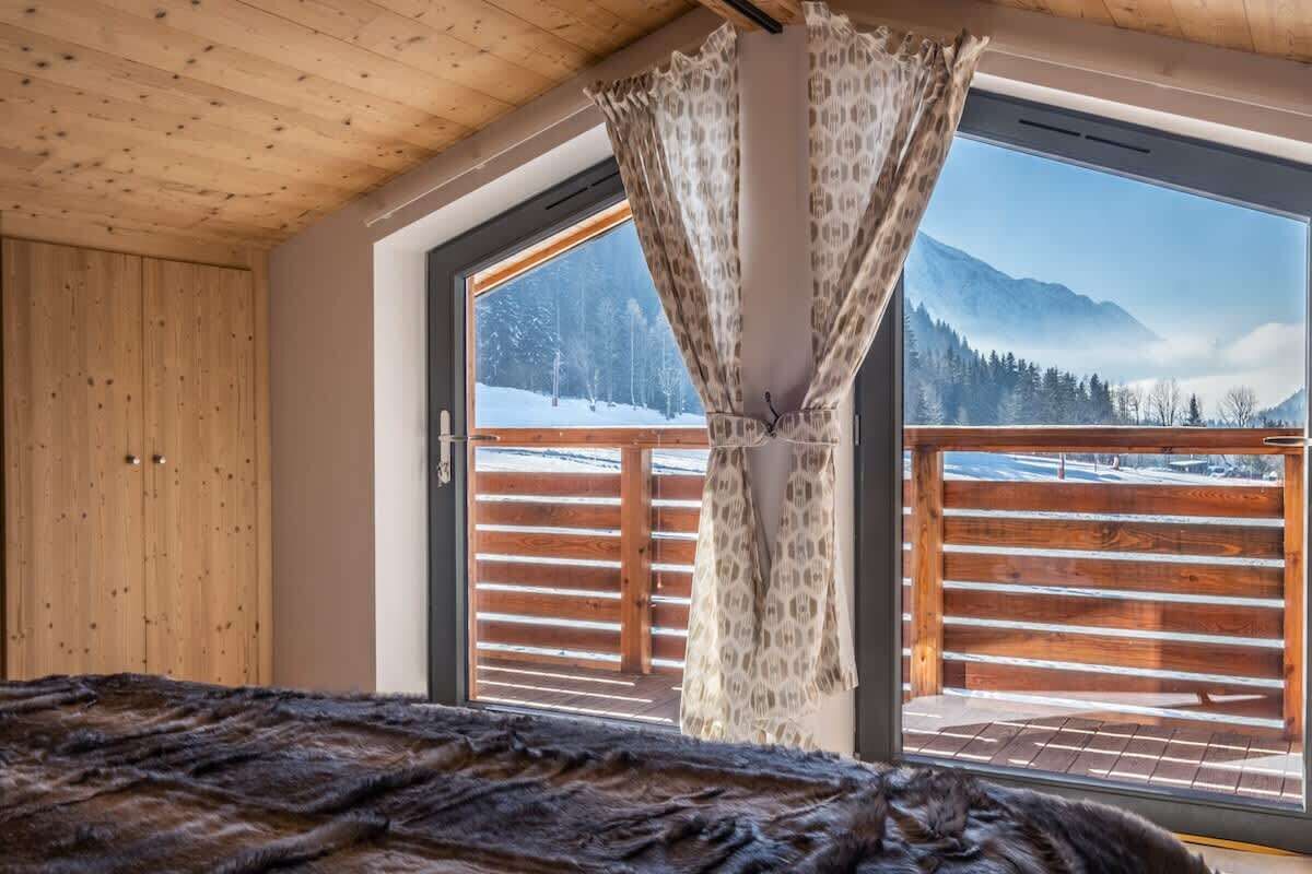 Een kamer met een groot raam, houten plafond en een bed met een gebloemd deken.
