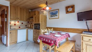 A cozy kitchen with wooden cabinets, a dining table set for four, a microwave, and a television.