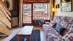Un cuarto acogedor con techo de madera, un sofá con tapicería estampada, una mesa de madera y vistas a un edificio de madera a través de una puerta de cristal.