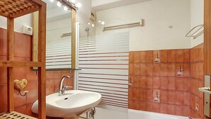 Un baño con un lavabo blanco, un espejo con iluminación y una ducha con puerta de vidrio, además de un estante de madera.