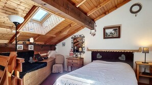 Un dormitorio acogedor en el ático, con techo inclinado, vigas de madera, tragaluces, una cama con cubrecama blanco, un aparador y una tocador con espejo.