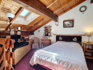 Enjoy a spacious room with a high ceiling, exposed beams, and a skylight. The room features a bed, a bench, a desk, and a mirror.