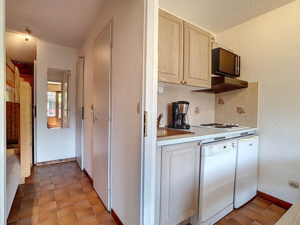 A compact kitchen with white cabinets, a coffee maker, and a dishwasher.