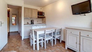 A compact kitchen with white cabinets, a microwave, a coffee maker, and a dining table with chairs.
