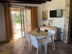A dining area with a round table, white chairs, a vase, and a television on the wall. - Residence Villa Felice (Lampedusa)