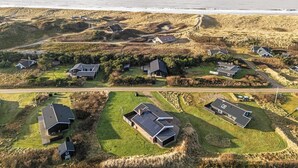 An aerial view of a coastal residential area with houses, some with solar panels, and a clear view of the ocean. - Lovely holiday home with pool, spa and sauna, only 200 meters from the North. (Harboøre)