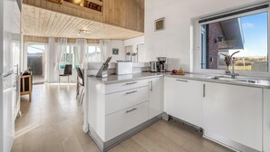 A modern kitchen with white cabinets, a large window, and a wooden ceiling. - Lovely holiday home with pool, spa and sauna, only 200 meters from the North. (Harboøre)