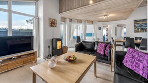 A modern living room with a large flat-screen TV, wooden ceiling, and a dining area with a table and chairs. - Lovely holiday home with pool, spa and sauna, only 200 meters from the North. (Harboøre)
