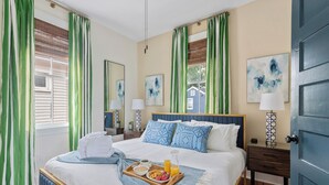 A neatly made bed with a tray of breakfast items, a bedside table with a lamp, and a door to the right. - Cozy Downtown Home | Wylde Jasmine (Charleston)