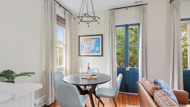 A dining area with a round table, four chairs, a chandelier, a framed picture, and a view through a blue door. - Cozy Downtown Home | Wylde Jasmine (Charleston)
