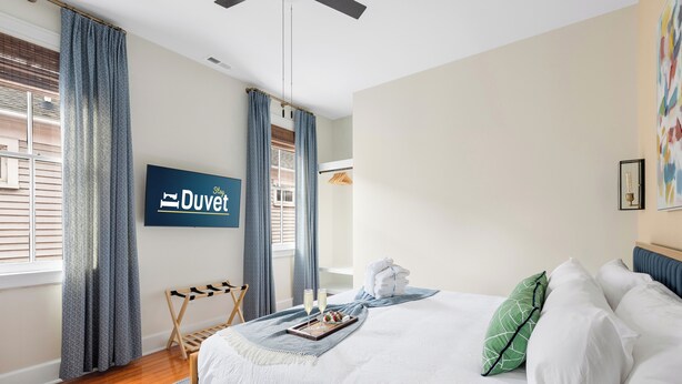 Habitación de hotel con una cama, una silla de madera, una bandeja con vasos y un postre, y un cartel en la pared.