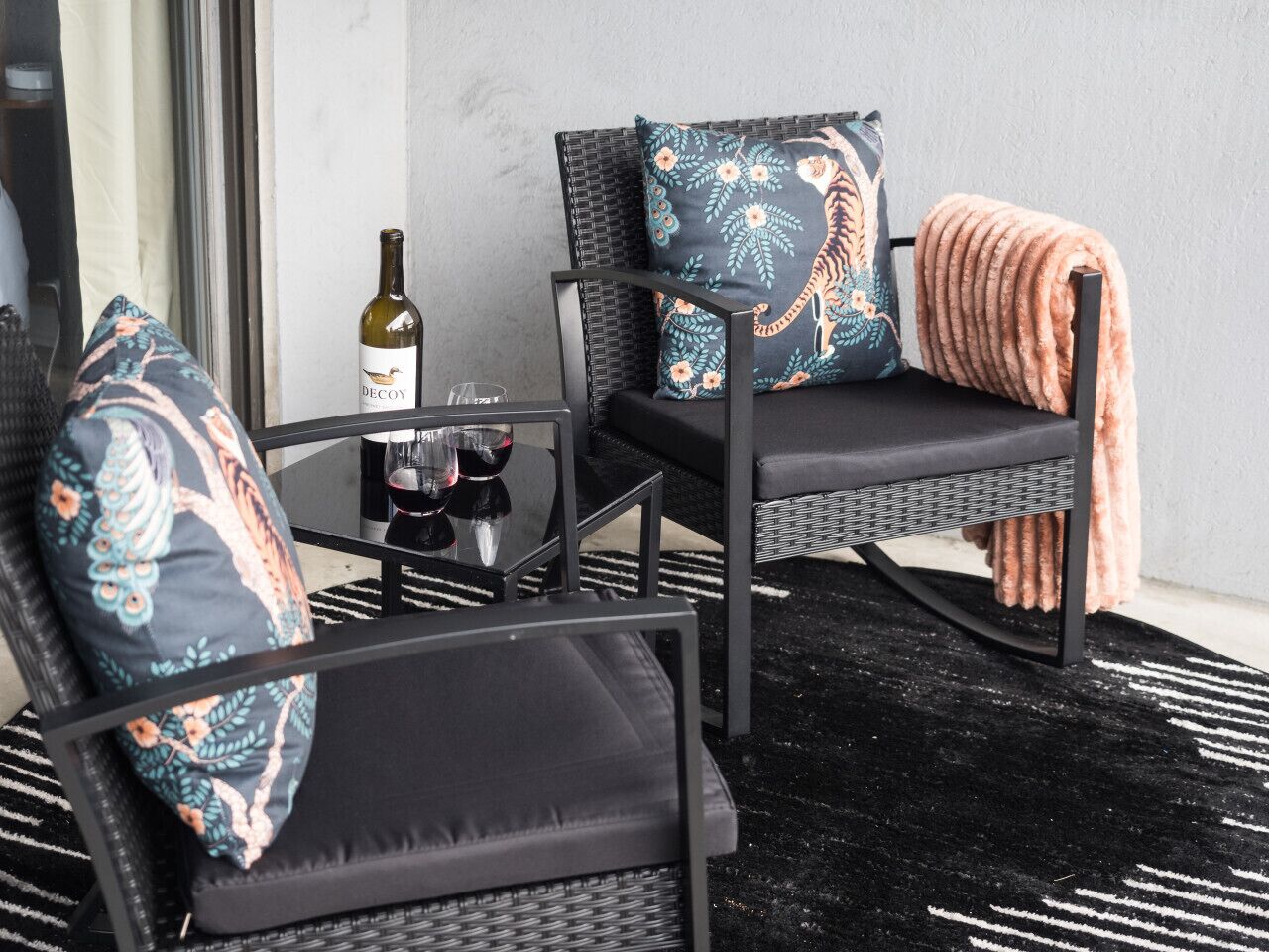 A seating area with two chairs and a table, a bottle of wine, and a blanket.