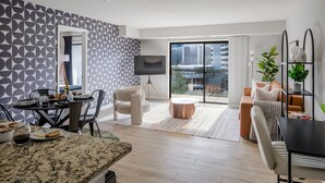 A modern living room with a dining area, a flat-screen TV, and a balcony with a city view.