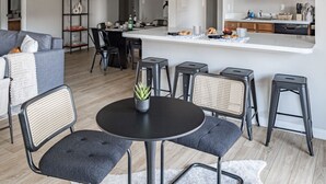 A modern kitchen with wooden cabinets, a central island, and a dining area with stools and a round table. - National Landing Spot Near Metro Sleeps 7 (Arlington)