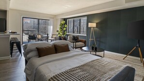 A hotel room with a large bed, a desk, a chair, a lamp, and a view of the city through large windows. - National Landing Spot Near Metro Sleeps 7 (Arlington)