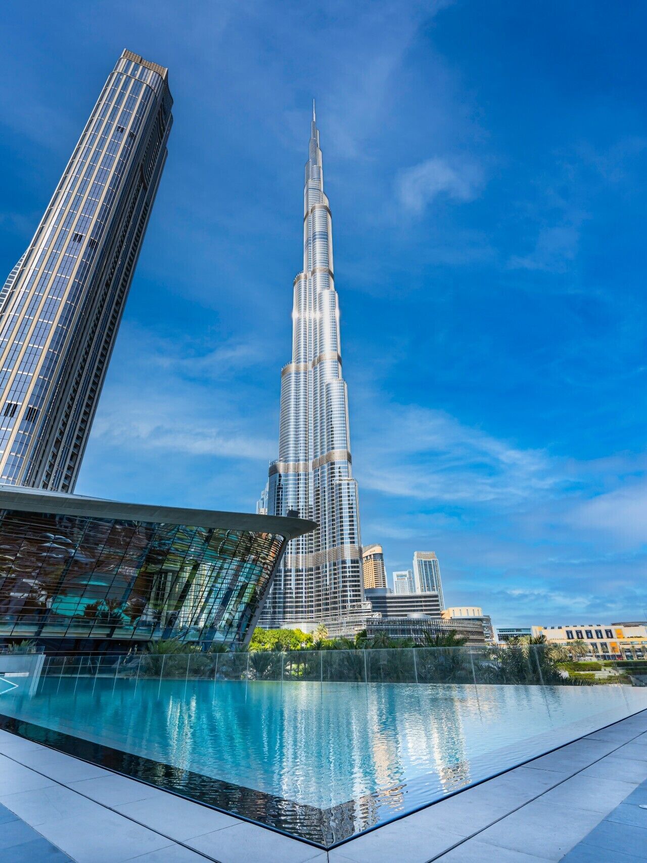 A modern skyscraper with a unique tapering design, surrounded by other high-rise buildings and a reflective pool.