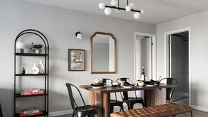 A dining area with a wooden table, black chairs, and a bench. There is a black metal shelf with plants and decorative items. A large mirror hangs on the wall, and a framed picture is visible. - Two bedroom  in United States of America, Arlington (Arlington)