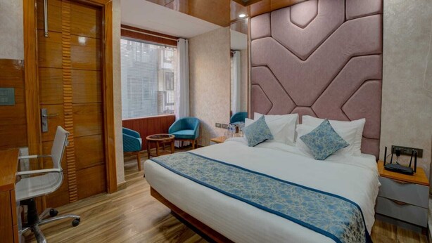 Ein Hotelzimmer mit einem großen Bett, einem Holztisch, einem Stuhl und einem Fenster mit Jalousien.