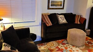 A living room with a dark brown sofa, a patterned rug, and a window with blinds.