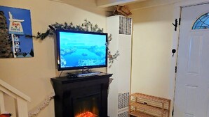 A living room with a fireplace, a television mounted above it, and a bench near the door.