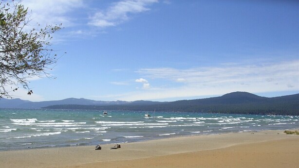 A beach with a sandy shore, calm sea, and distant mountains.