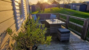 Een houten terras met tuinmeubilair, een kleine boom en uitzicht op een woonwijk.