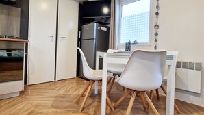 Een kleine keuken met een koelkast, een eettafel met twee stoelen en een raam dat voor natuurlijk licht zorgt.