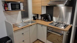 Een kleine keuken met een magnetron, fornuis, spoelbak en een houten aanrecht.