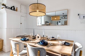 Un comedor con una mesa de madera dispuesta para seis personas, rodeada de sillas. Un espejo grande cuelga sobre la mesa, reflejando la habitación.