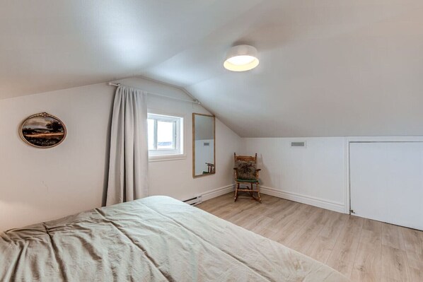 Un dormitorio con cama, una silla, un ventanal, un espejo y una puerta.
