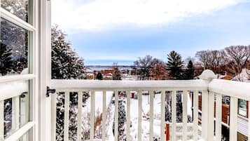 A snow-covered balcony with a view of a residential area and a body of water in the distance.
